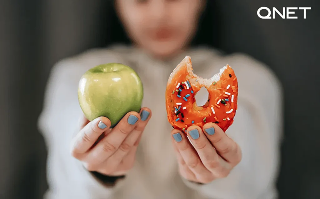 Woman showing apple and bitten doughnut | QNET India