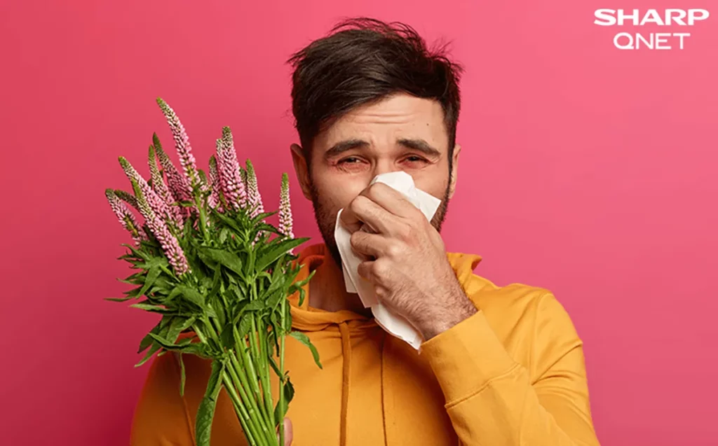An Indian man holding flowers and covering his nose due to pollen allergy symptoms